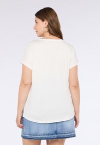 Top alb cu mânecă scurtă, cu o croială lejeră și un decolteu rotunjit, asortat cu o fustă din denim cu un tiv desfăcut și cusături decorative.