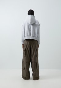 Avkortad grå hoodie med ett strukturerat mönster och luva, kombinerad med löst sittande mörkgröna cargobyxor med flera fickor.