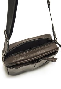 Bolso cruzado hecho de cuero texturizado de color gris oscuro, con dos compartimentos con cremallera y una correa ajustable. Presenta acentos de hardware mínimos.