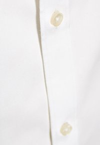 Wit overhemd met kraag gemaakt van gladde stof, voorzien van afgeronde, lichtgekleurde knopen en een netjes gestikte plooi.