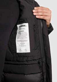 Sort pufferjakke indvendig med et plejebadge, lynlåslomme og glat tekstur. Har en skinnende sort foring og vandret quiltning.