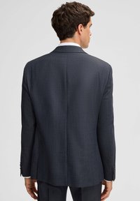 Donkergrijs colbert met een gestructureerd patroon, smalle pasvorm, enkele split, en revers met inkeping, voorzien van knoopmanchetten en strakke lijnen.