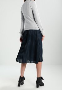 Šedé tričko s dlouhým rukávem a vysokým límcem spojené s tmavou plisovanou midi sukňou. Oblečení doplňují černé kotníčkové boty s mašlemi.