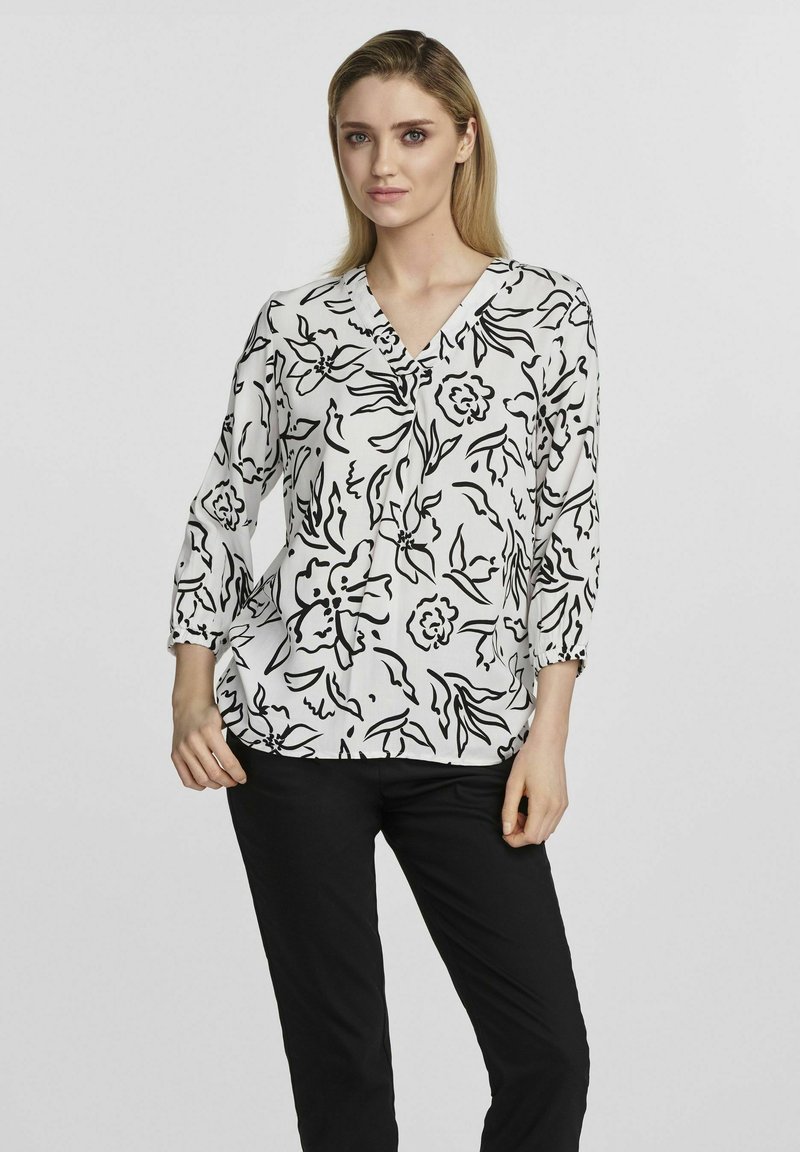 Bluzka w kwiatowy wzór w czerni i bieli, dekolt w serek, rękawy do łokcia, lekki materiał, zestawiona z czarnymi spodniami.