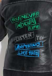 Schwarze Lederjacke mit auffälligem Text in Grün, Grau und Blau auf der Rückseite, mit strukturierter Oberfläche und sichtbaren Nähdetails.