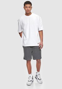 T-shirt en coton blanc à manches courtes, coupe ample, associé à un short en maille gris charbon avec un logo de marque. Des baskets blanches et noires complètent le look.
