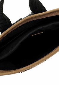 Top view of an open small brown and black tote bag showing its empty black interior and black fabric handles.