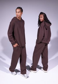 Sudaderas con capucha y joggers de gran tamaño en algodón suave, con un corte holgado y bolsillos, combinados con zapatillas deportivas plateadas.