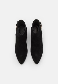 Stivali alla caviglia in suede nero con punta affilata, chiusura laterale con zip e accenti in metallo dorato. Texture liscia e design minimalista.
