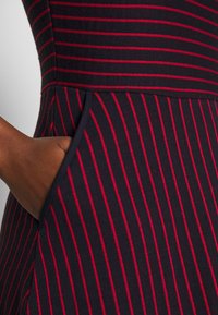 Gestreiftes Kleid mit einem figurbetonten Oberteil in Marineblau und Rot, das horizontale Streifen, gerippte Textur und eine Seitentasche aufweist.