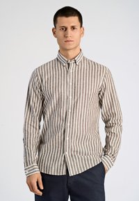 Camisa de botones de manga larga con estrechas rayas verticales en marrón y blanco, hecha de un tejido texturizado. Presenta un cuello tipo camisa y cierre de botones.