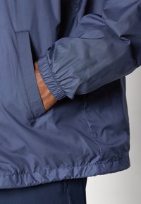 Navy blue lightweight jacket featuring elastic cuffs and side pockets, made from a smooth, water-resistant fabric with a minimal design.