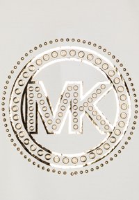 Metalický logo se zkratkou "MK" v kruhovém designu, obklopené malými kulatými nýty, na světle texturovaném pozadí.