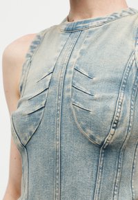 Αμάνικη γαλάζια μπλούζα από acid-wash τζιν με δομημένες ραφές και πιεταριστές λεπτομέρειες στο στήθος.