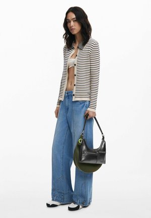 Striped ribbed cardigan in cream and navy, wide-legged denim pants, black and green handbag, and white shoes with black accents.