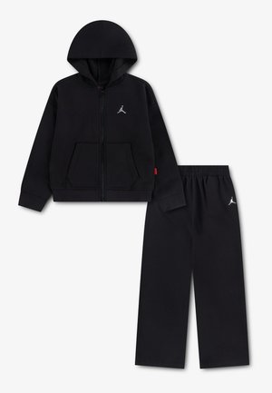 Musta hupparivetoketjullinen pusero ja siihen sopivat mustat housut, joissa on valkoiset Jumpman-logot, aseteltu tasaisesti valkoiselle taustalle.