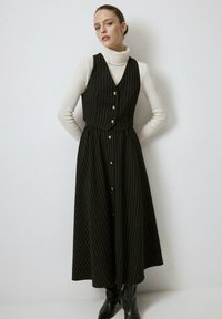 Black and white striped long dress with a fitted bodice, button detailing, and a flowing skirt. Paired with a white turtleneck and black boots.