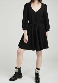 Svart klänning med V-hals, lång ärm och figurnära midja. Kombinerad med svarta kängor i combat-stil med pärlprydnader på ärmsluten.