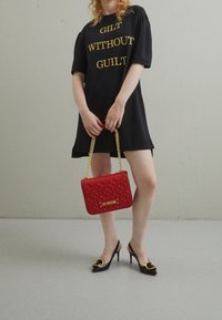 Černé šaty s krátkým rukávem a zlatým nápisem, červená prošívaná kabelka se zlatým řetězem a černé lodičky na jehlovém podpatku se zlatými akcenty.