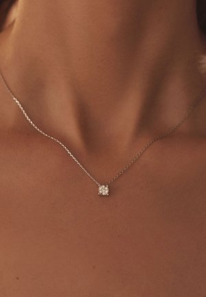 Zilveren ketting met een vierkante hanger met meerdere fonkelende stenen, rustend op een gladde hals.