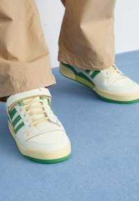 Sneakers da tennis con tomaia in pelle bianca e verde, caratterizzati da tre strisce verdi, lacci color crema e una suola verde testurizzata.