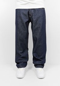 Loose-fitting dark blue denim jeans with a straight leg design, featuring standard pockets and paired with white sneakers.