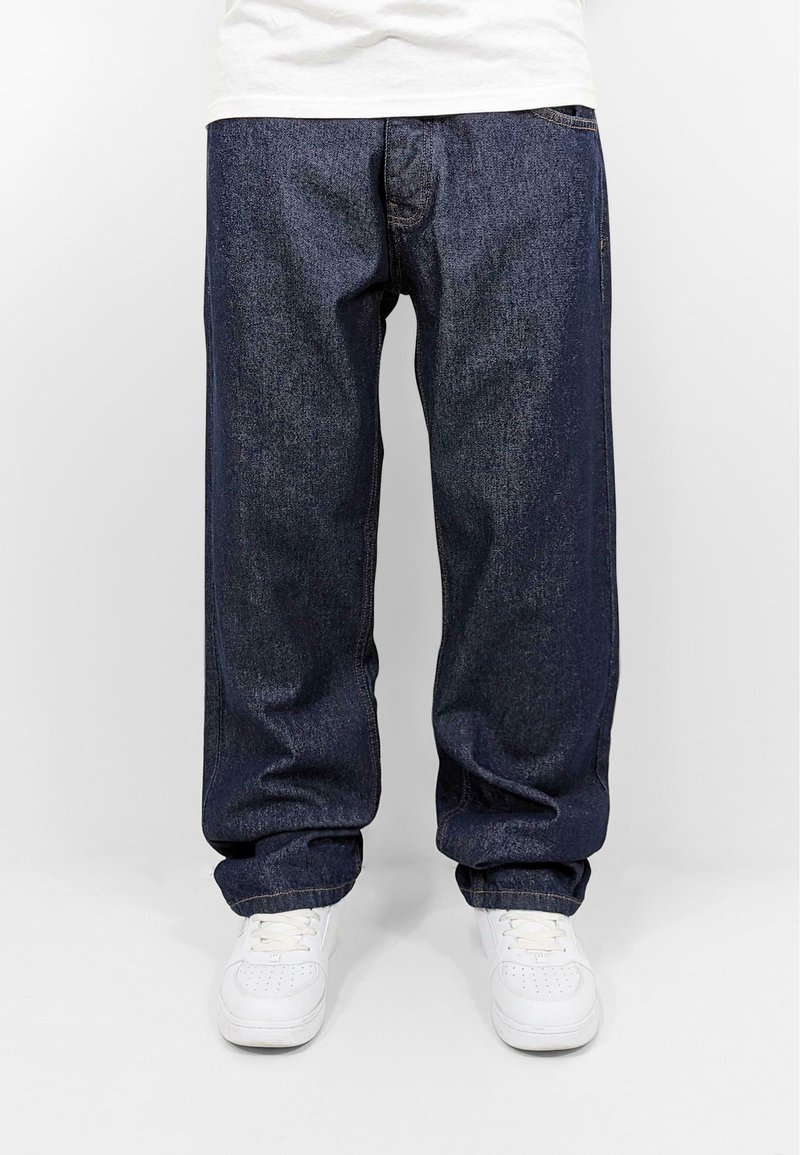 Loose-fitting dark blue denim jeans with a straight leg design, featuring standard pockets and paired with white sneakers.