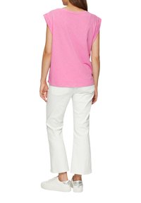 Lichtroze top met korte mouwen en oprolbare mouwen, gecombineerd met witte flared jeans en witte sneaker met een zilveren accent op de achterkant.