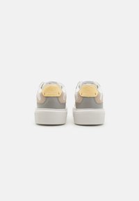 Stiilsed sneakers, millel on segatud materjalide disain, sealhulgas valge nahk, hall seemisnahk ja kollased aktsendid. Paksud valged kummist tallad.