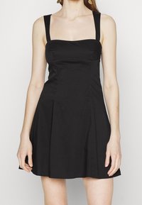 Svart klänning med en figursydd överdel, breda axelband och veckad kjol. Tillverkad av ett mjukt tyg med en enkel, minimalistisk design.