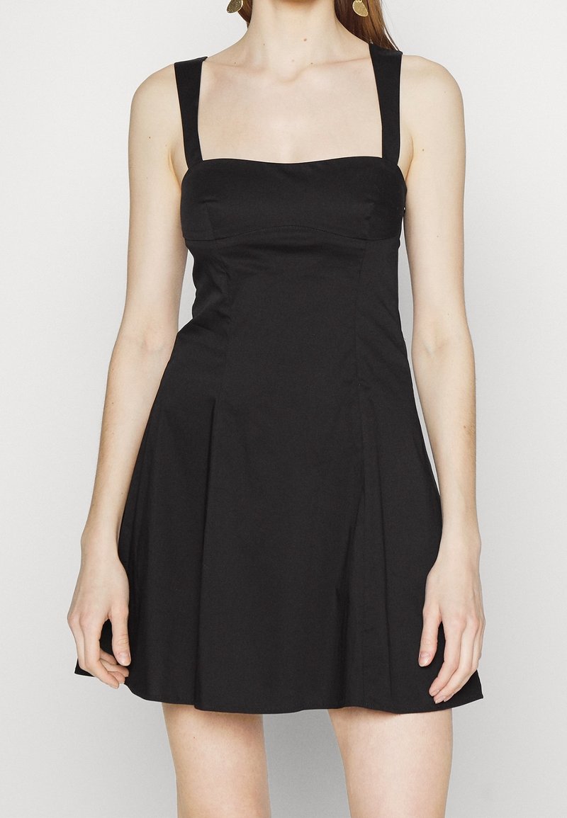 Svart klänning med en figursydd överdel, breda axelband och veckad kjol. Tillverkad av ett mjukt tyg med en enkel, minimalistisk design.