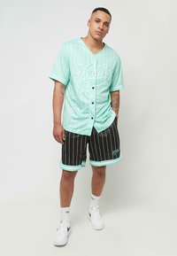 Minti zaļš beisbola krekls ar baltām svītrām, melnas šortus ar vertikālām svītrām un baltām akcentiem. Stilizēts ar baltām sporta apaviem.