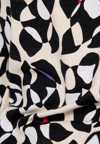 Black and white abstract geometric pattern on fabric with small red and purple accents, slightly wrinkled.