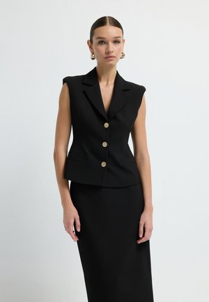 Blazer negro sin mangas con un ajuste entallado, botones dorados y solapas afiladas. Tela suave con un diseño minimalista, acompañado de una falda a juego.