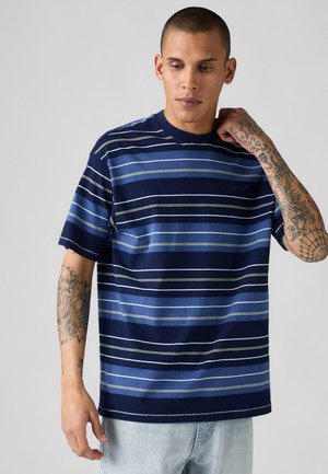 Short-sleeve navy and blue striped t-shirt with a crew neck. Features thin white and light green stripes. Model wears light jeans.