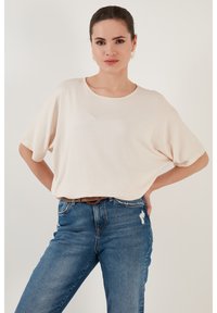 Světle růžové oversized tričko s krátkými rukávy a kulatým výstřihem, spárované s modrými розtrhanými džíny a hnědým opaskem. Hladká textura.