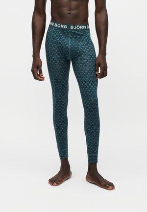 Mannequin masculin portant des leggings bleus à motifs sur toute la longueur avec une ceinture à logo Björn Borg, debout pieds nus sur un fond uni.