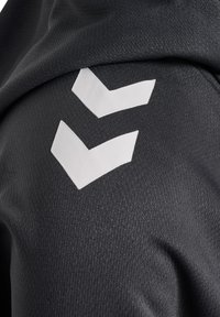 Twee witte chevronvormen gedrukt op donkergrijze gestructureerde stof, mogelijk onderdeel van een kledingstuk.