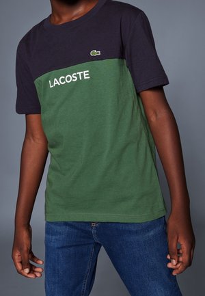 Kurzärmeliges T-Shirt in Marineblau und Grün, mit weißem "LACOSTE"-Schriftzug und einer kleinen Logoapplikation auf der Brust. Aus Baumwolle, reguläre Passform.