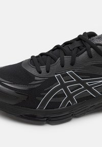 Chaussure de sport noire avec tige en mesh, semelle épaisse, lacets noirs et logo de marque gris contrastant sur le côté.
