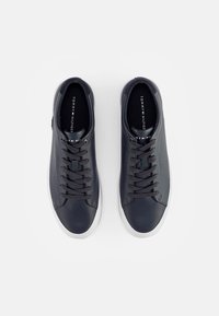 Baskets montantes en cuir noir avec une semelle en caoutchouc blanc. Présentent des lacets plats, une texture lisse et un logo "TOMMY HILFIGER" sur la languette.