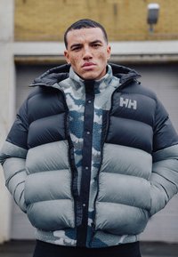 Pufferjack met grijze en zwarte secties, voorzien van een ritssluiting aan de voorkant, een capuchon en een gestructureerde blauwe patroon binnenfleece laag.