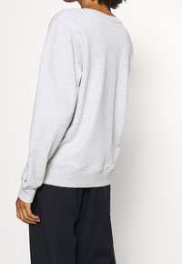 Šedá mikina s volným střihem, žebrovanými manžetami a lemem. Měkká textura a minimalistický design s malým logem na rukávu.