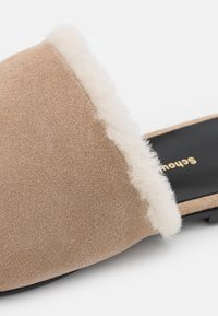 Chaussure taupe en daim à enfiler avec doublure blanche duveteuse et semelle intérieure noire avec texte doré imprimé.