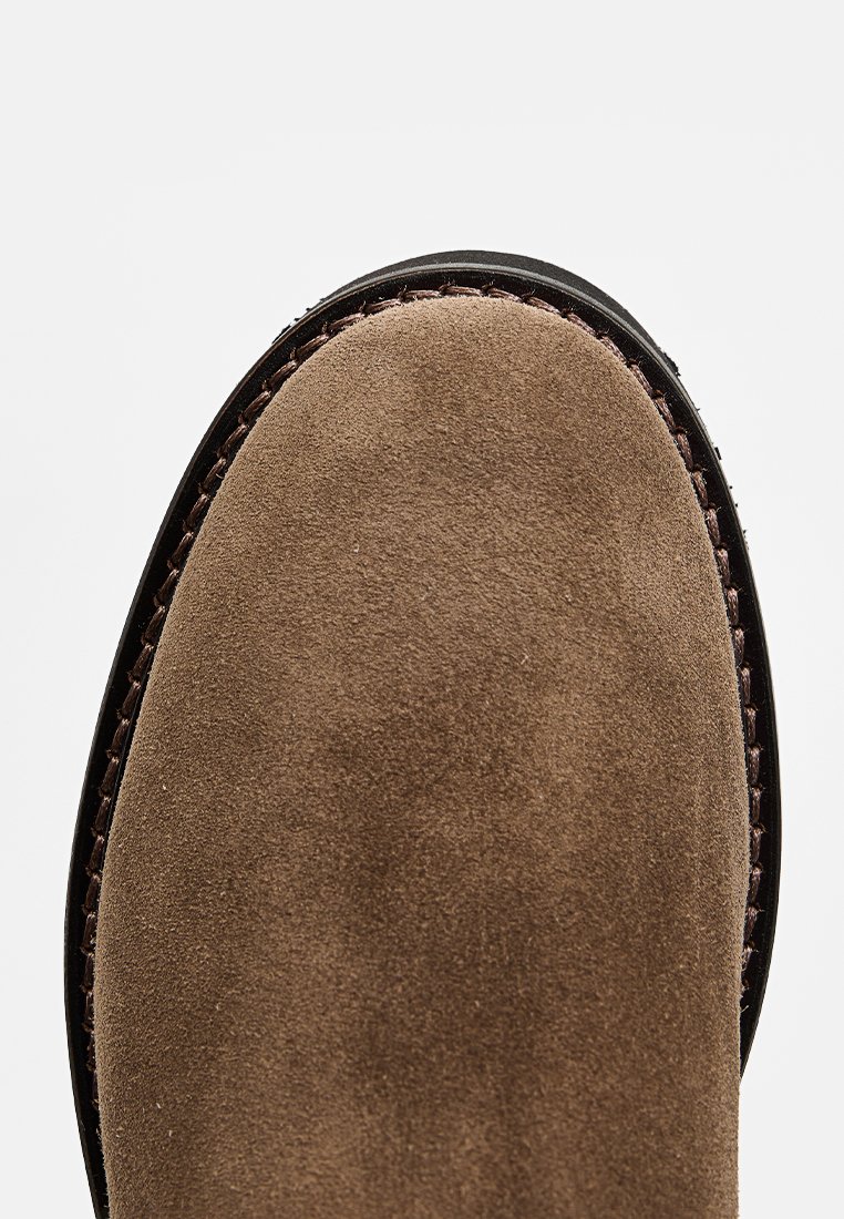 Brauner Wildlederstiefel mit abgerundeter Spitze und dunkler Sohle. Verfügt über eine strukturierte Oberfläche und dunkle Nähte entlang der Kante.