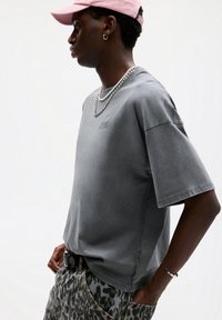 Grå oversized t-shirt i bomuld med logo-print, parret med leopardprintede shorts, sølv kædedyse og en pink kasket.