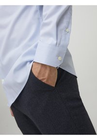 Jasnoniebieska koszula z guzikami o teksturowym wykończeniu, z białymi guzikami i zrolowanymi rękawami, zestawiona z ciemnymi, teksturowanymi spodniami slim-fit.