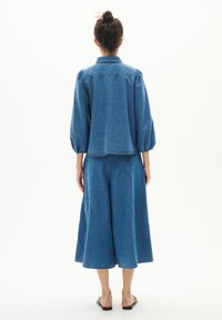 Farmerdzseki puffos ujjakkal és gallérral, széles lábú farmer culottes-szal párosítva. Mindkét ruhadarab középkék színű, látható varrással.