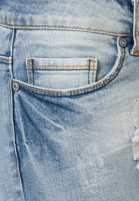 Light blue denim jeans featuring a classic five-pocket design, visible distressed areas, and contrasting tan stitching.