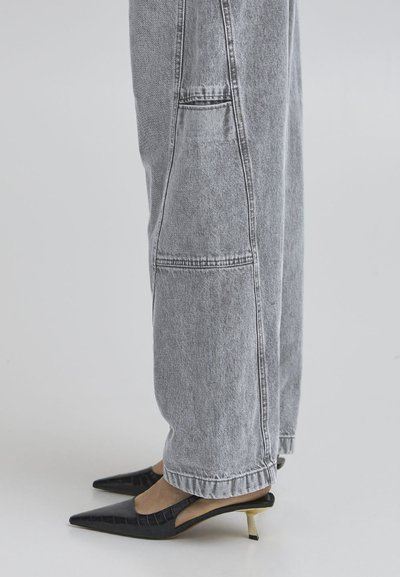 Gray denim wide-leg trousers with a relaxed fit and visible stitching details, paired with black pointed-toe slingback heels featuring gold accents.